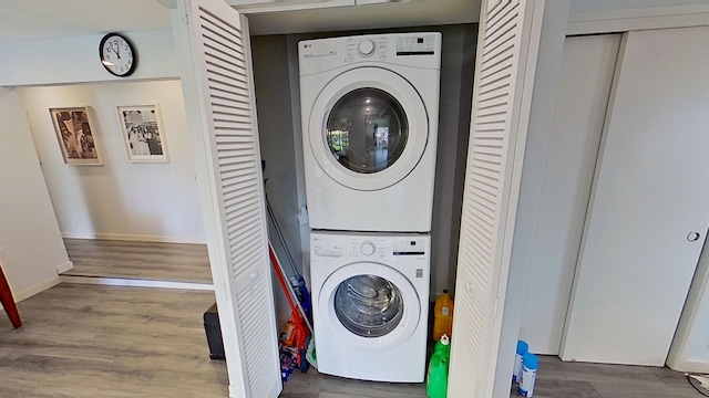 clothes washing area featuring stacked washer and clothes dryer, baseboards, laundry area, and wood finished floors