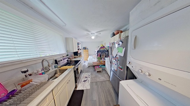 kitchen featuring stacked washer and dryer, stainless steel range with electric cooktop, light wood finished floors, white cabinets, and a ceiling fan