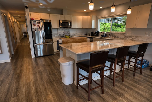 kitchen with dark wood-style flooring, light stone countertops, appliances with stainless steel finishes, and a peninsula