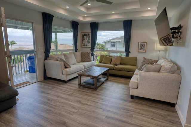 living area with a ceiling fan, a raised ceiling, wood finished floors, and a wealth of natural light
