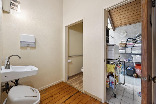 bathroom featuring toilet, a sink, wood finished floors, wooden ceiling, and baseboards