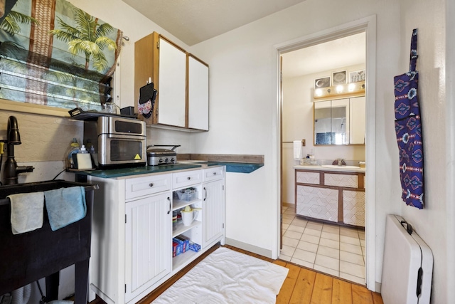 kitchen featuring light wood finished floors, white cabinets, dark countertops, open shelves, and a sink