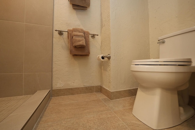 bathroom featuring toilet, tile patterned flooring, a tile shower, and a textured wall