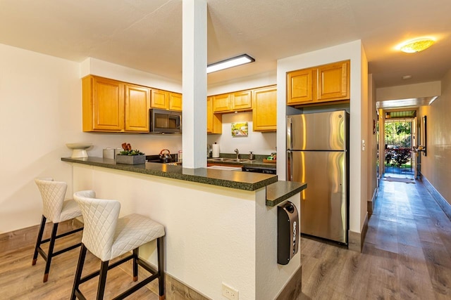 kitchen featuring kitchen peninsula, dark hardwood / wood-style flooring, sink, stainless steel refrigerator, and a breakfast bar area