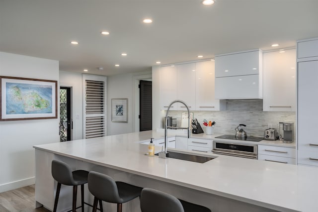 kitchen with white cabinetry, a kitchen bar, light wood-type flooring, and sink