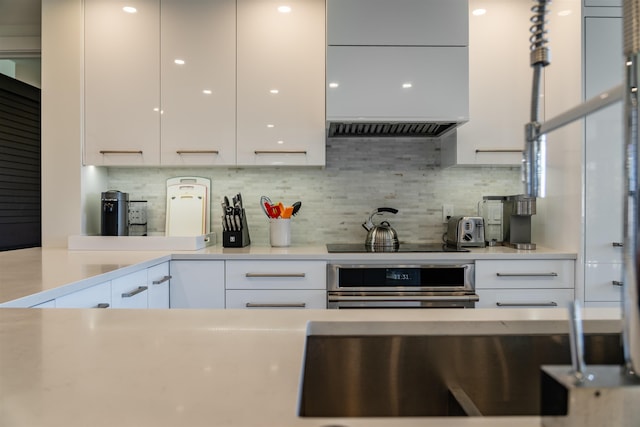 kitchen with stainless steel oven, ventilation hood, black electric cooktop, tasteful backsplash, and white cabinetry