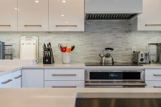 kitchen featuring white cabinetry, stainless steel oven, and wall chimney range hood