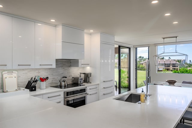 kitchen featuring black electric cooktop, pendant lighting, white cabinets, oven, and a breakfast bar area