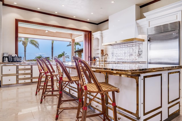 kitchen with white cabinetry, built in fridge, light stone counters, and custom exhaust hood