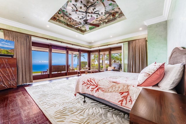 bedroom with access to outside, a water view, hardwood / wood-style floors, and a tray ceiling