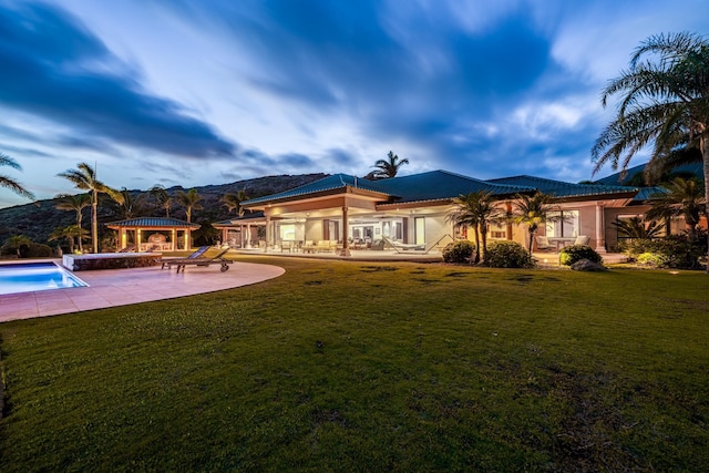 back of property with a mountain view, a patio area, and a yard