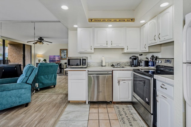 kitchen featuring stainless steel appliances, tile counters, open floor plan, white cabinets, and a sink