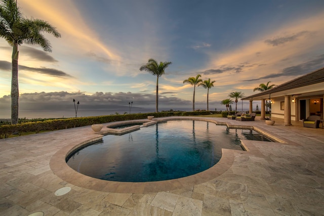 pool at dusk with an in ground hot tub and a patio