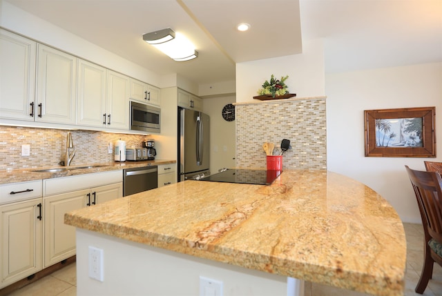 kitchen with light stone countertops, stainless steel appliances, sink, kitchen peninsula, and decorative backsplash