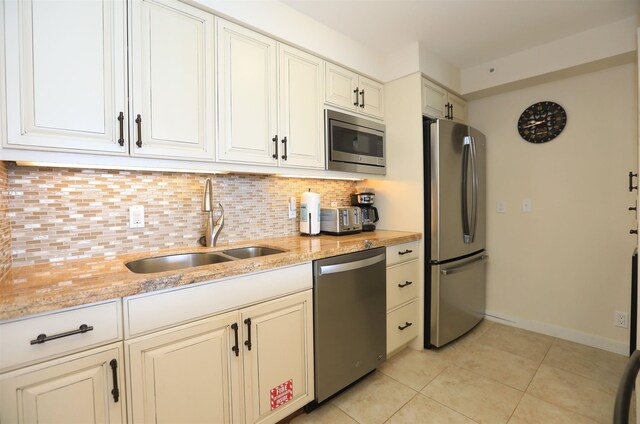 kitchen with light tile patterned floors, appliances with stainless steel finishes, tasteful backsplash, sink, and light stone counters