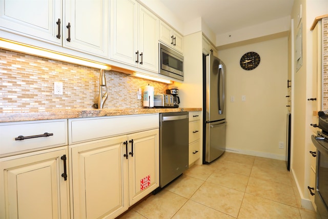 kitchen featuring stainless steel appliances, light stone counters, light tile patterned floors, and backsplash