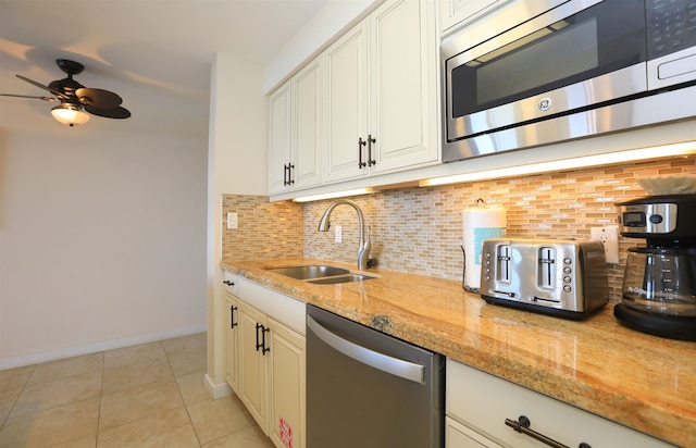 kitchen with tasteful backsplash, stainless steel appliances, light stone counters, sink, and ceiling fan