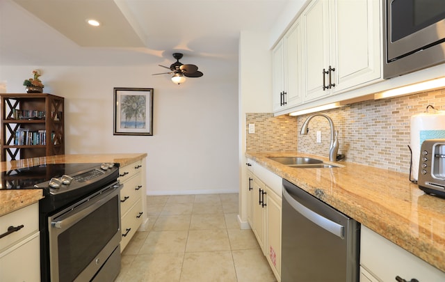 kitchen featuring white cabinets, appliances with stainless steel finishes, light stone counters, sink, and ceiling fan