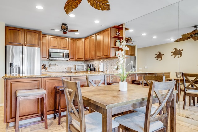 kitchen with appliances with stainless steel finishes, ceiling fan, light stone countertops, and light tile flooring