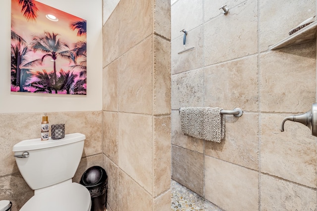 bathroom featuring tiled shower, toilet, and tile walls