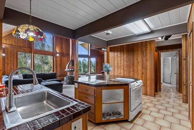 kitchen with sink, wood walls, a center island, tile counters, and white range with gas cooktop