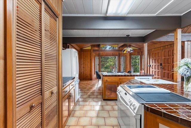 kitchen featuring wood walls, beamed ceiling, sink, hanging light fixtures, and white appliances