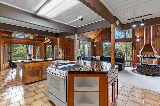 kitchen with tile countertops, white electric range, wooden walls, hanging light fixtures, and a center island