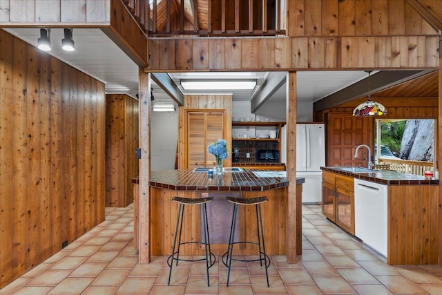 kitchen with sink, white appliances, backsplash, wooden walls, and tile counters