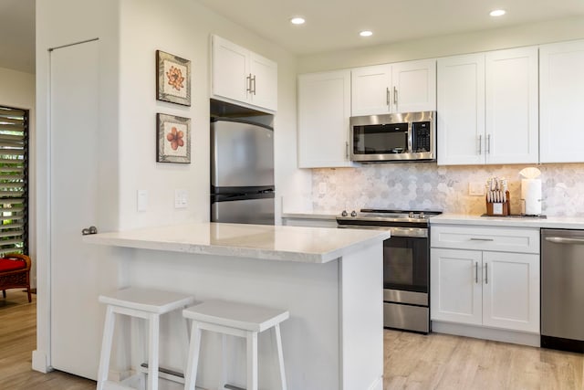 kitchen featuring white cabinets, light hardwood / wood-style flooring, appliances with stainless steel finishes, tasteful backsplash, and kitchen peninsula