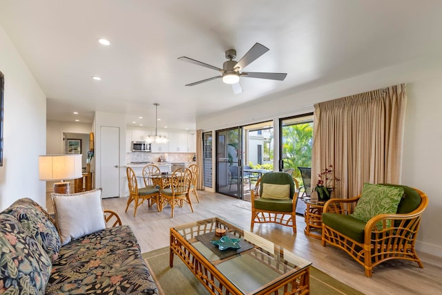 living room with ceiling fan with notable chandelier and light hardwood / wood-style flooring