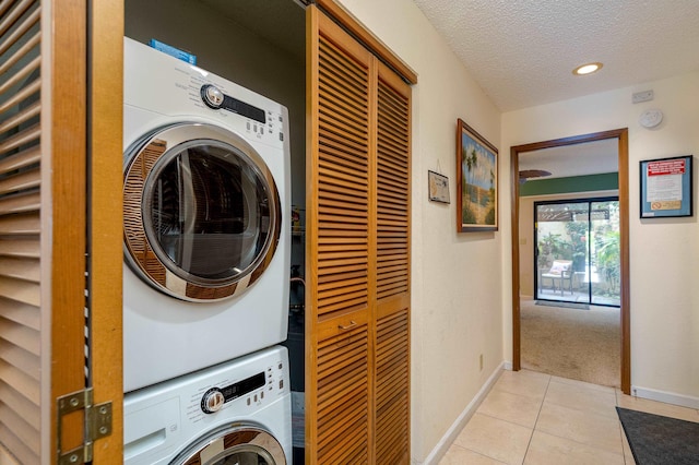 laundry area with stacked washer / dryer, light tile patterned floors, and a textured ceiling