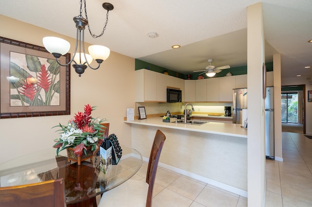 kitchen featuring sink, kitchen peninsula, stainless steel fridge, light tile patterned flooring, and ceiling fan with notable chandelier