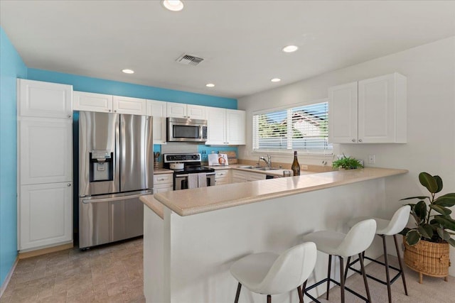 kitchen featuring stainless steel appliances, sink, white cabinetry, kitchen peninsula, and a breakfast bar