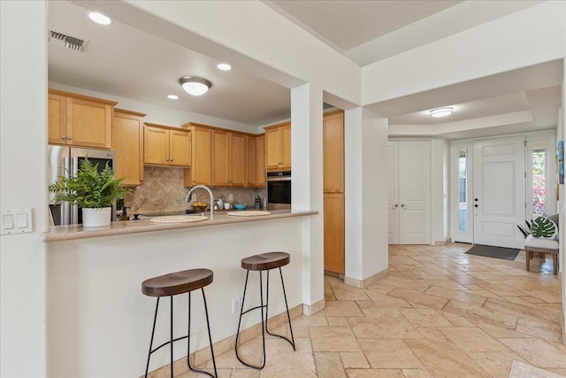 kitchen with sink, stainless steel appliances, tasteful backsplash, a kitchen breakfast bar, and kitchen peninsula