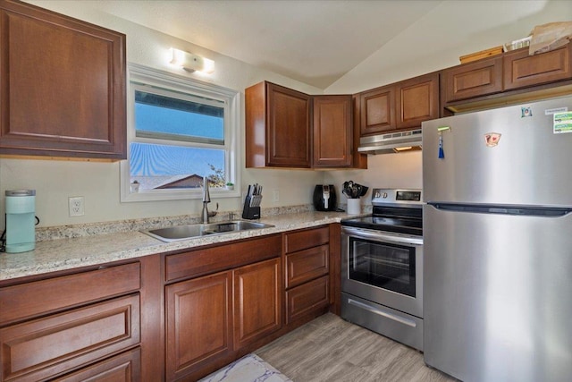 kitchen featuring lofted ceiling, sink, light stone counters, appliances with stainless steel finishes, and light hardwood / wood-style floors