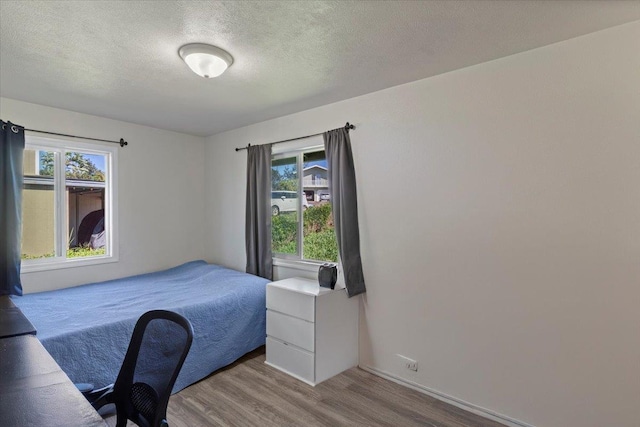 bedroom with multiple windows, a textured ceiling, and light hardwood / wood-style floors