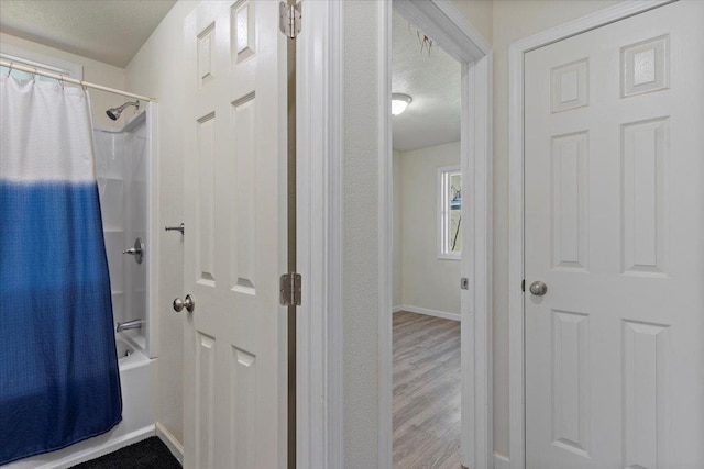 bathroom featuring shower / bathtub combination with curtain, wood-type flooring, and a textured ceiling