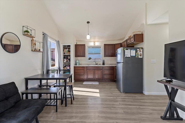 kitchen with sink, stainless steel fridge, hanging light fixtures, vaulted ceiling, and light wood-type flooring