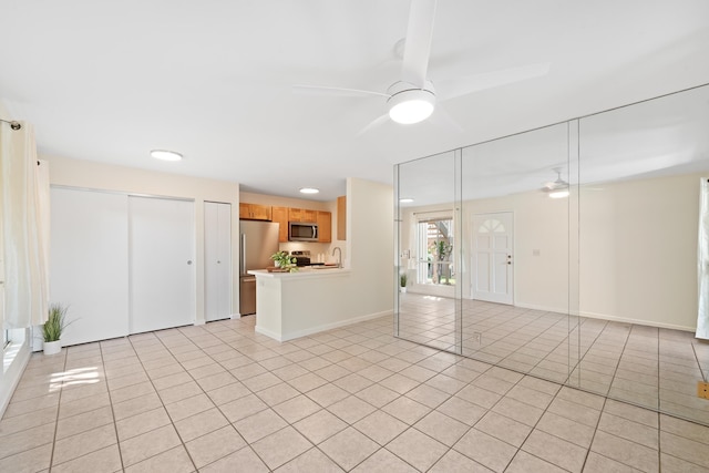 unfurnished living room with light tile patterned floors, ceiling fan, baseboards, and a sink