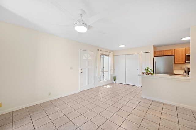 unfurnished living room featuring light tile patterned flooring, a ceiling fan, and baseboards