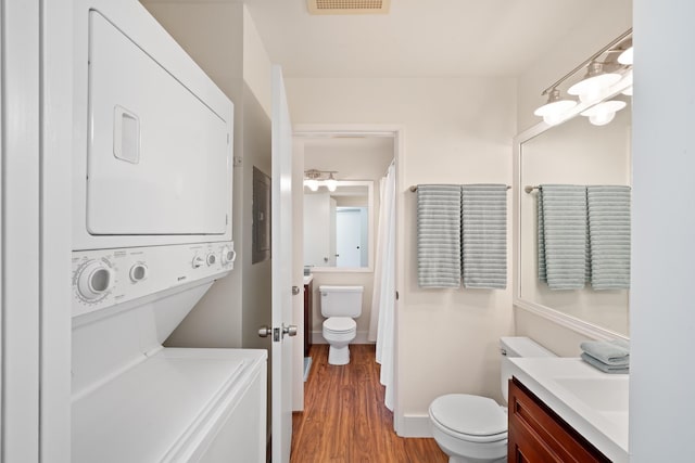 bathroom with stacked washer and clothes dryer, toilet, wood finished floors, vanity, and electric panel