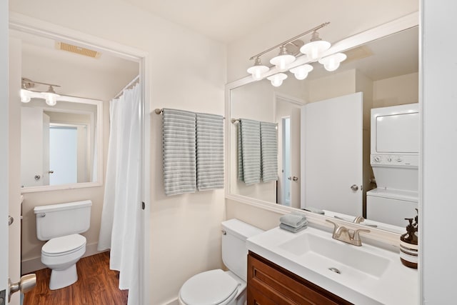 full bathroom with stacked washer / drying machine, toilet, wood finished floors, and vanity