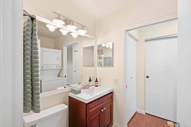 bathroom with stacked washing machine and dryer, toilet, vanity, and wood finished floors