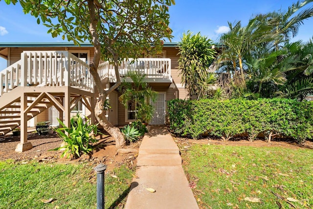 view of front of home with a deck, stairs, and a front lawn