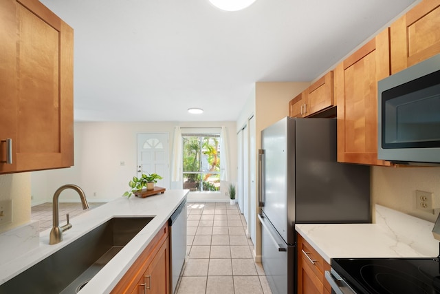kitchen featuring stainless steel appliances, a sink, light tile patterned floors, brown cabinets, and light stone counters
