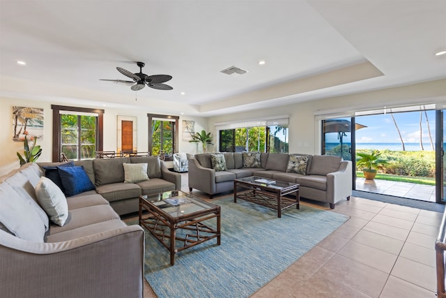 tiled living room featuring a raised ceiling, a healthy amount of sunlight, and ceiling fan