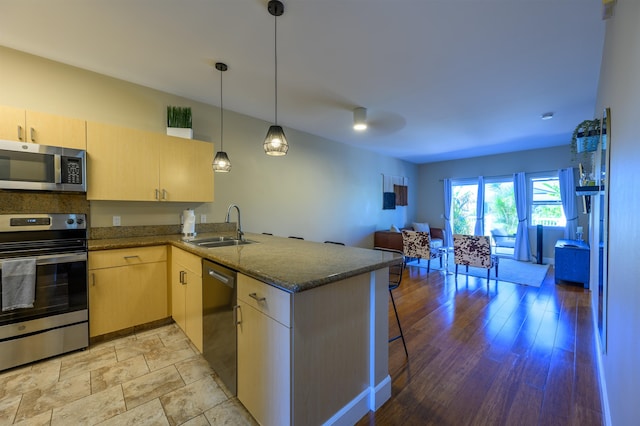 kitchen with hanging light fixtures, stainless steel appliances, sink, light brown cabinets, and kitchen peninsula