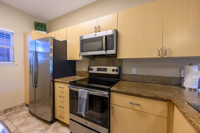 kitchen with dark stone countertops, light brown cabinetry, and stainless steel appliances