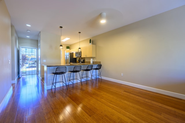 kitchen with hardwood / wood-style floors, white cabinetry, kitchen peninsula, hanging light fixtures, and a breakfast bar