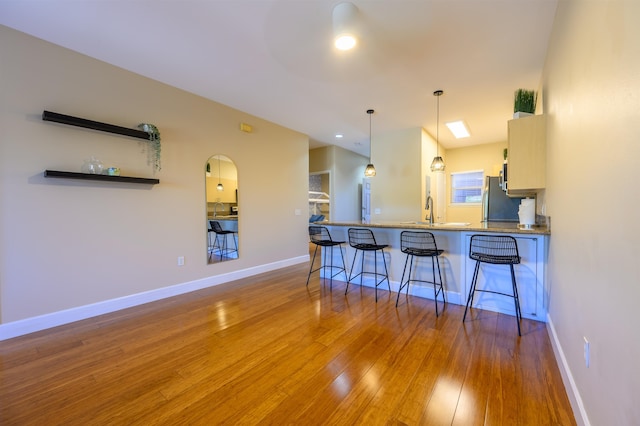 kitchen with stainless steel refrigerator, decorative light fixtures, kitchen peninsula, hardwood / wood-style flooring, and a breakfast bar area